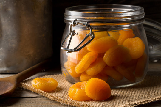 Whole dried apricots fruit in storage jar on dark wooden table