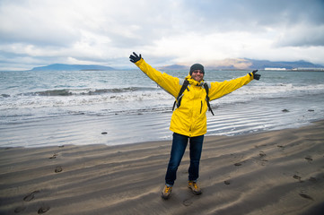 Happy man on sea beach in reykjavik, iceland. Man traveler smile with raised arms on sea shore....