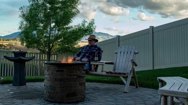 Wide angle timelapse of a guy sitting by a fire pit in the back yard zoming in to the flame