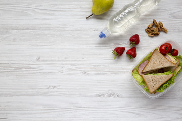 Healthy school lunch box with fresh organic vegetables sandwiches, walnuts, bottle of water and fruits on white wooden background, flat lay. From above. Top view. Space for text.
