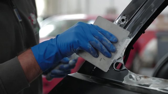 Close up, mechanic rubs white glue on car