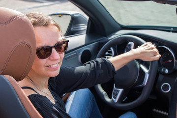 Beautiful young woman happy to drive her convertible car on a sunny day. she looks at camera. -...