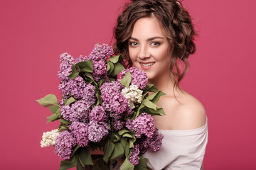 A young slender girl in stylish clothes is holding a bouquet of purple flowers. She is surprised at the gift she was given on a date. On a pink background with space for text