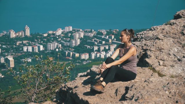 Traveler Woman Sits on Top of a Rocky Mountain. Landscape with mountains and cross on peak on a small town and the sea. Mount Stavrikai. Yalta, Crimea. Achieving the goal. Forward movement, motivation