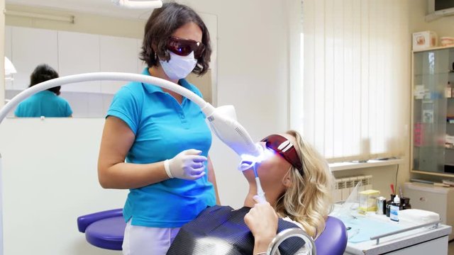 4k video of dentist talking to patient lying in dentist chair during teeth whitening procedure
