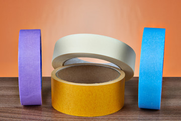 Several multi-colored rolls of adhesive tape on an orange background.