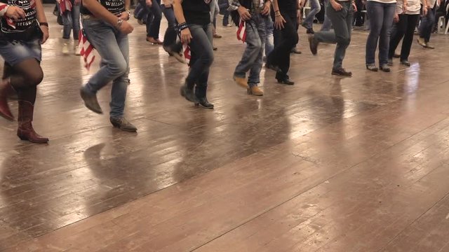 People dancing a western choreography at a folk festival. Country dancers moving together. Denim, cowboy boots and USA flag. Learning line dance, bluegrass music and tradition of America