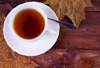 cup of tea and maple leaves in the background on a wooden