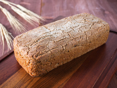 Homemade bread on a wooden cutting board and a nearby wheat stalk