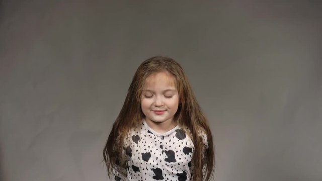 Happy little girl in the studio on a gray background. She jumps, shows different emotions. Hair fluttering from the wind. Super slow motion, shot at 180fps.