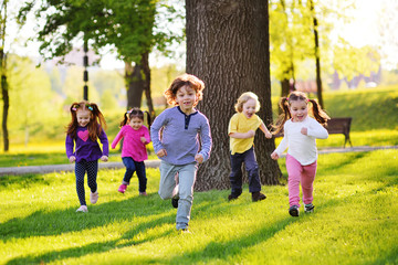 many young children smiling running along the grass in the park. Childhood, Children's Day, vacation, vacation, adventure, friendship. - obrazy, fototapety, plakaty