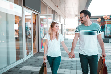 Happy young couple holding hands and walking along street with shopping bags