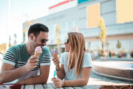 A beautiful young couple are siting on a bench and eating ice-cream on the street