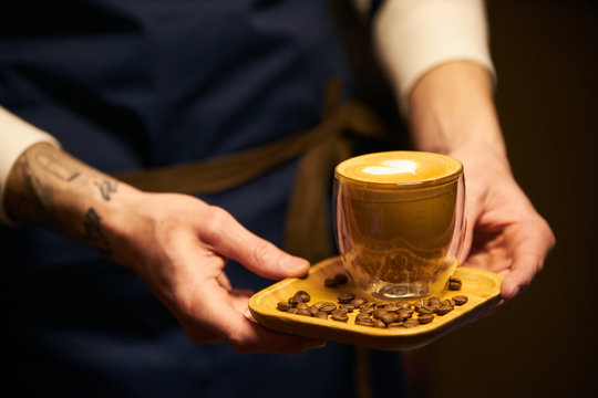 Barista in dark apron uniform holding a cup of coffee with latte art