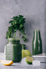 Green smoothie in jar with apple,baby spinach, parsley and banana, over a green round plate on a gray board against a gray background with parlsey leaves.
