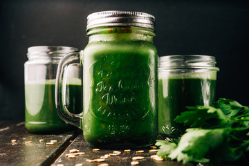Green smoothie in  mason jars with apple,baby spinach, parsley and banana, on a wooden  board against a dark  background.