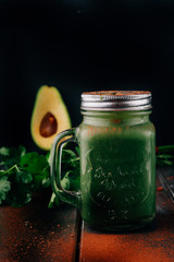Green smoothie in jar with apple,avocado, and banana,on a wooden  board against a dark  background with chocolate powder.