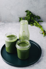 Green smoothie in jar with apple,baby spinach, parsley and banana, over a green round plate on a gray board against a gray background with parlsey leaves.