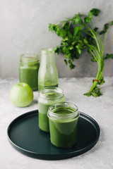 Green smoothie in jar with apple,baby spinach, parsley and banana, over a green round plate on a gray board against a gray background with parlsey leaves.