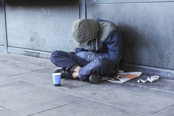 Homeless man sitting on the street in the shadow of the building and begging for help and money....