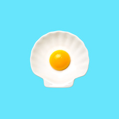Egg yolk on white shell plate on blue background. Top view. Minimalistic design, colorful background