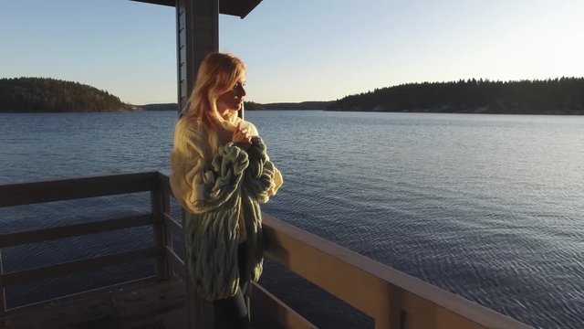 beautiful woman is standing on a pier by the lake at sunset