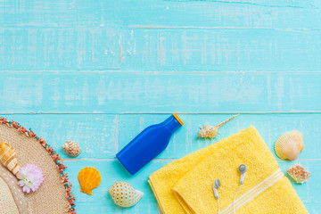 Beach accessories including sunglasses, sunscreen, hat beach, shell, yellow towel and Earphone on bright blue pastel wooden background for summer holiday and vacation concept.