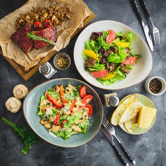 Grilled ribs with buckwheat, salad with citrus and grilled chicken liver, salad with tomato and vine in a glass. Table with food in restaurant.