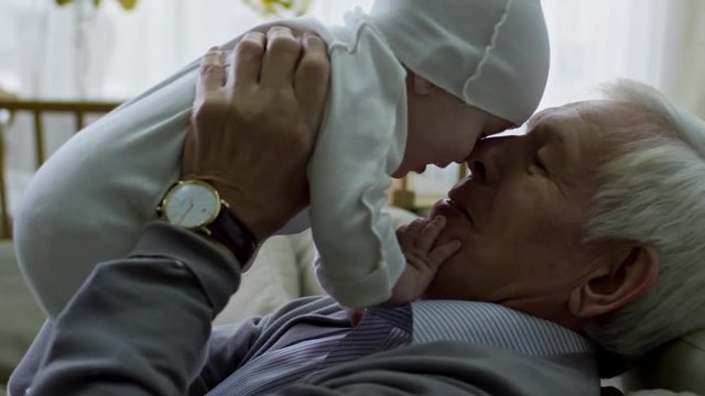 Tilt up of happy grandfather with grey hair playing with adorable baby boy while babysitting