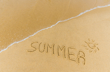 Ocean sea waves on the beach in a resort city running over the caption summer written on the sand. Concept of summer, holidays, vacation, travel, and beach