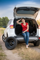 Young woman sitting in open car trunk waiting for auto service to change flat tire