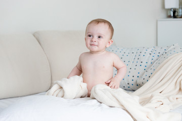 Cute baby boy sitting on big bed at bedroom