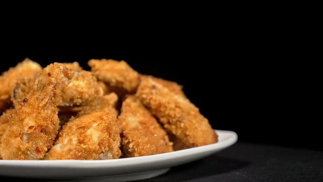 Cool beautiful fresh juicy cooked chicken wings in breading rotate on turntable. Buffalo wings spread on food white plate in table. Very tasty and beautiful. Cooking with deep fryer fry machine.