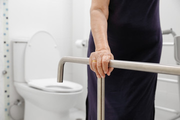 Elderly woman holding on handrail in toilet.