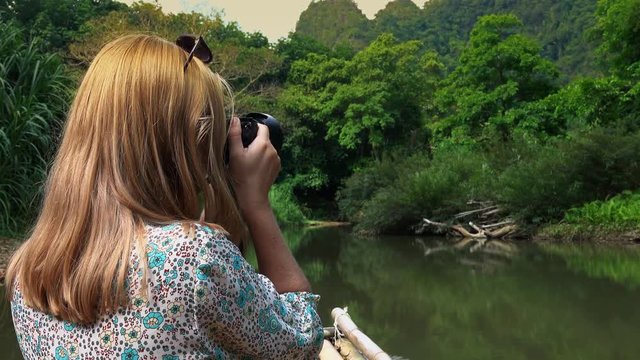 Young Woman Taking Photos Sailing on Bamboo Raft across Tropical River Among Lush Greenery