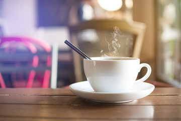 White cup of hot drink with steaming  on table with bokeh background at coffee shop