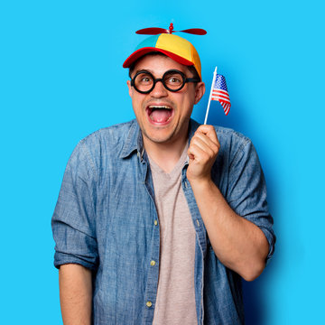 Young nerd man with noob hat holding an American flag on blue background