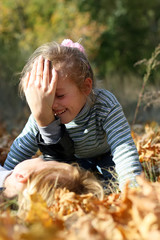 Naklejka premium A woman with a smiling little girl are playing on the ground covered by yellow foliage