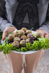 Woman hands holds vegan black beans falafel balls with salad leaves, basil, onion, tomato ketchup hot sauce served for lunch or dinner. Vegetarian healthy food