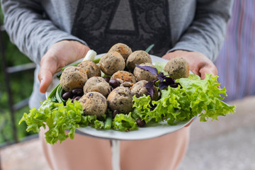 Woman hands holds vegan black beans falafel balls with salad leaves, basil, onion, tomato ketchup hot sauce served for lunch or dinner. Vegetarian healthy food