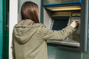 Fototapeta na wymiar A young woman takes money from an ATM. Grabs a card from the ATM. Finance, credit card, withdrawal of money.