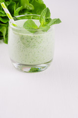 Summer healthy food - green vegetable smoothies with leaf mint, greens, straw on white wood background. Vertical, closeup.