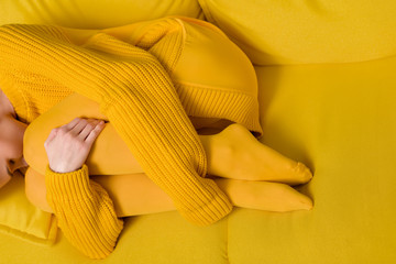 partial view of woman in yellow sweater and tights sleeping on yellow sofa