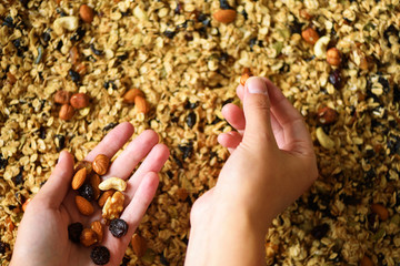 Female hand holds granola against the background of baking sheet with granola. Food for breakfast. Meal background and macro texture