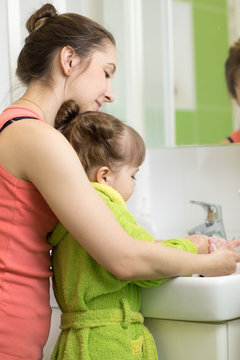 child girl and her mother washing hands with soap in bathroom