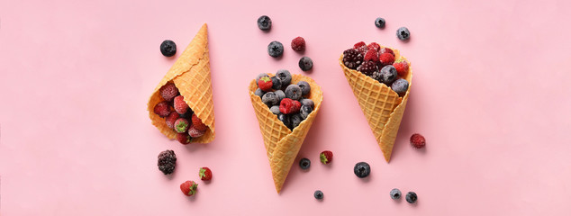 Obraz na płótnie Canvas Frozen berries - strawberry, blueberry, blackberry, raspberry in waffle cones on pink background. Top view. Banner. Pattern for minimal style. Pop art design, creative concept