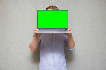 young guy in shirt, holding laptop with green screen in front of him