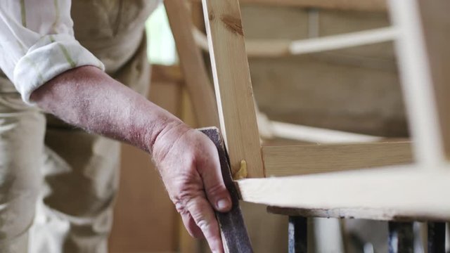 Slow motion shot of elderly man carpenter builds a small boat with his hands out of wood in a small workshop