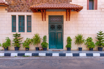 Facade of the clock tower in Montaza public park with green wooden door with red tile canopy above and window shutters on stone bricks wall, Alexandria, Egypt