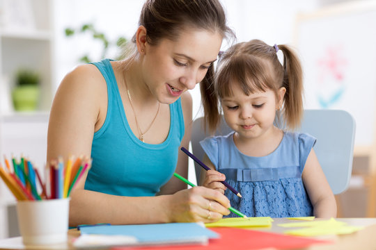 Kindergarten teacher and kid girl drawing lessons at school